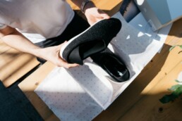 Image of an unboxing video featuring black athletic shoes. The unboxing video is being filmed from an overhead view.